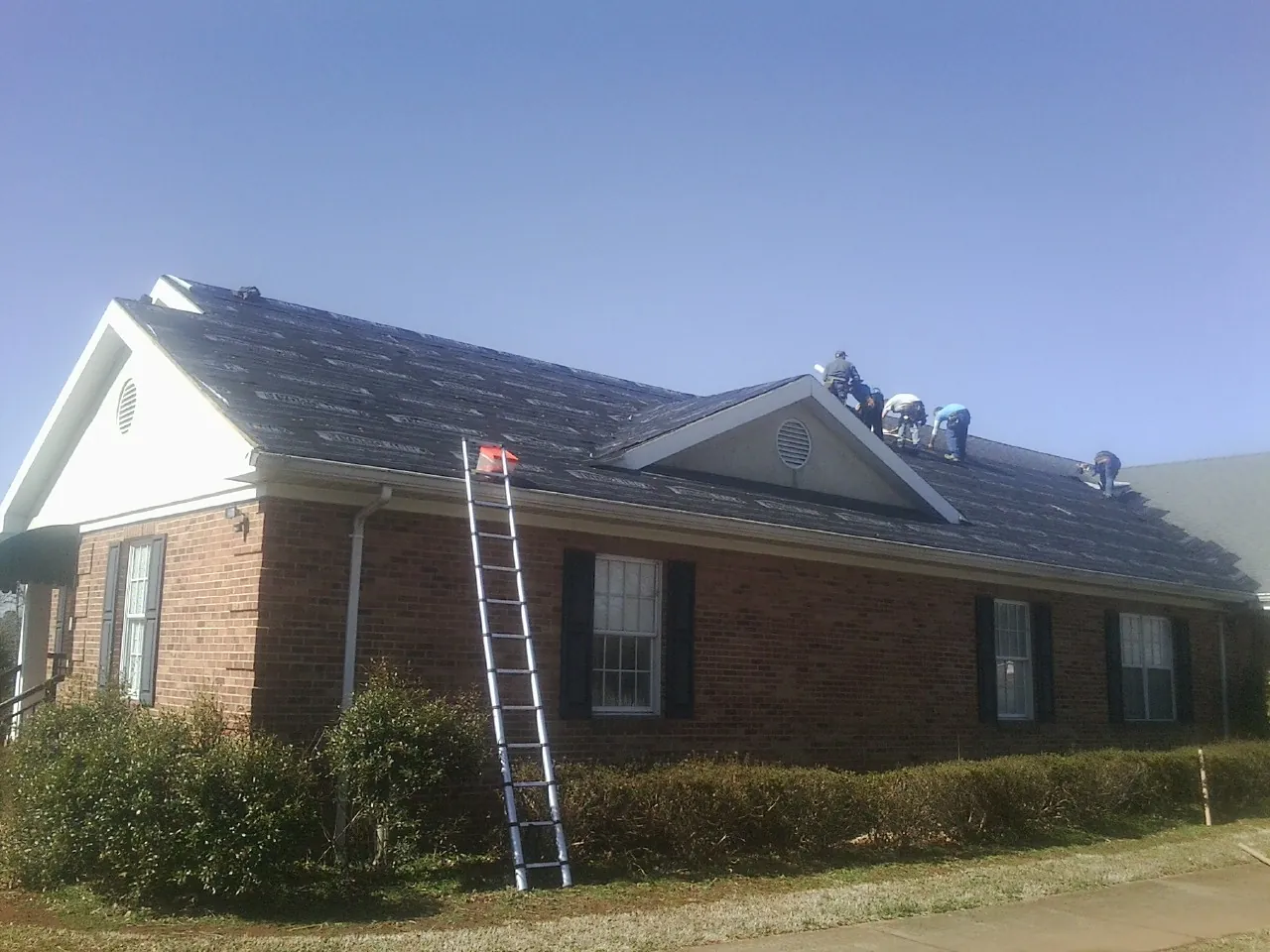 Crew tearing shingles off a brick ranch roof with a ladder set — Metal Roof Repair work by our crew in Mcville