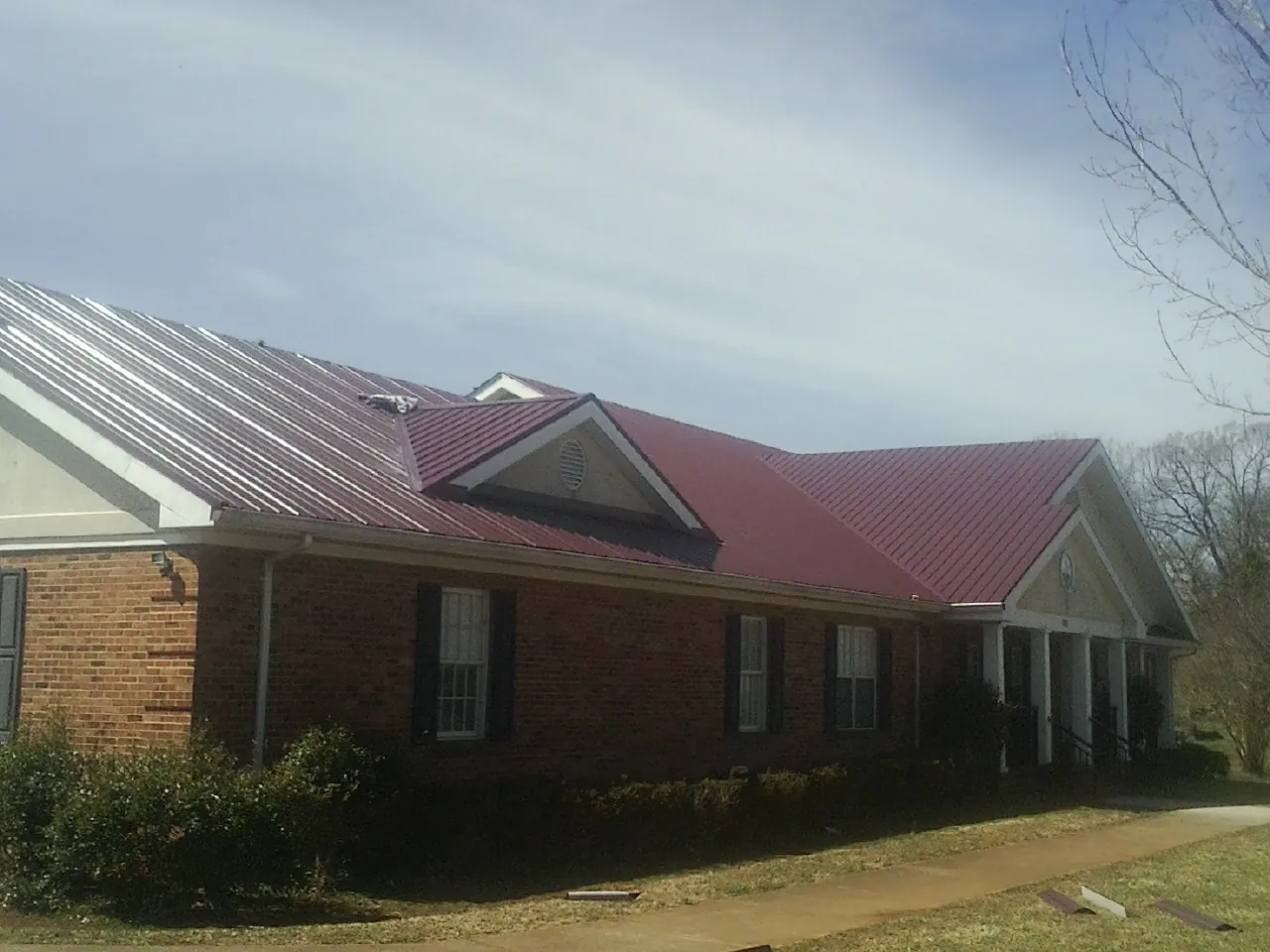 Red metal roof with gabled entries on a long brick building, from a Hail Damage Roof Repair job in Mcville