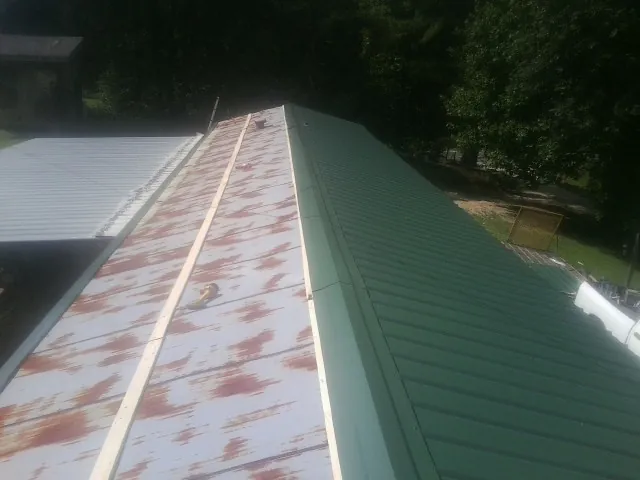Old rusted panels beside newly installed green metal roofing — Wind Damage Roof Repair by Roofing Brothers in Mcville