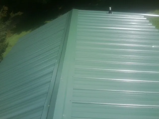 New green metal panels meeting at the ridge of a roof — Flat Roof Repair work by our crew in Mcville