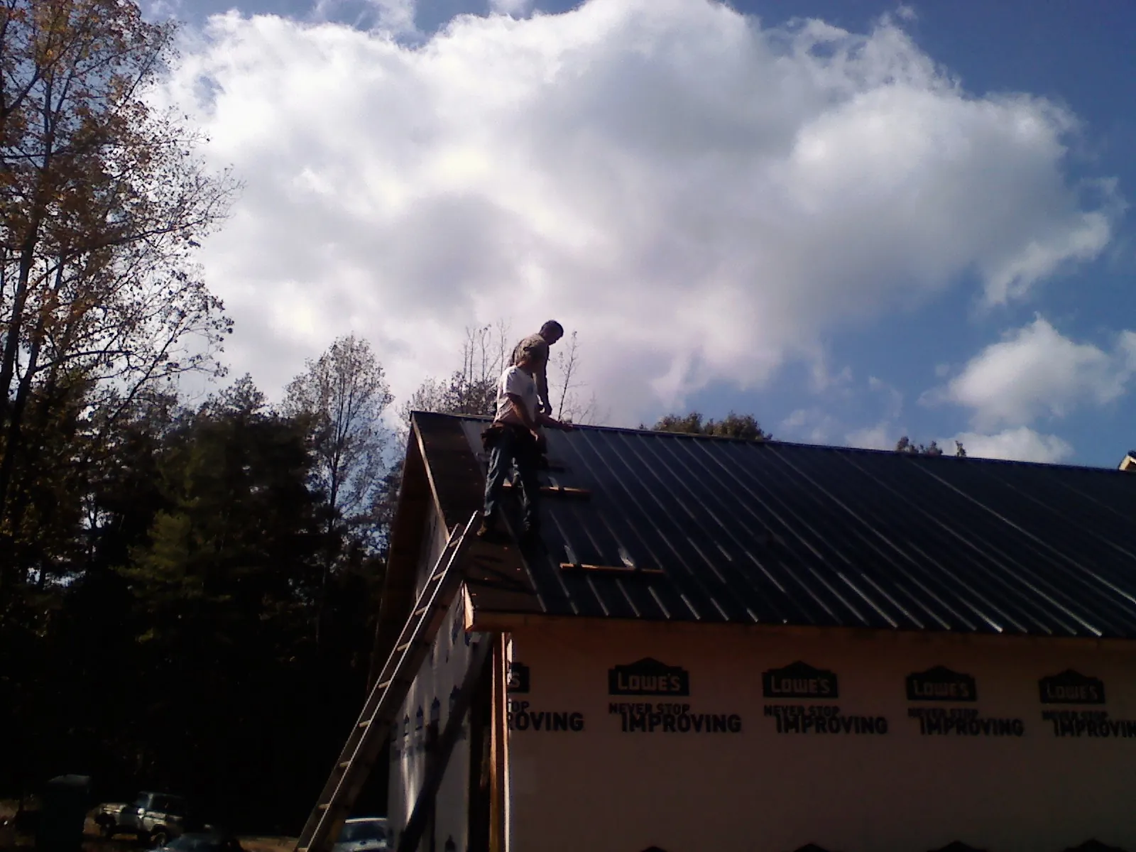 Roofer fastening dark metal panels high against a cloudy sky, from a Roof Inspection job in Mcville